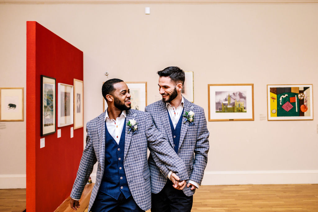 Wedding couple hold hands in front of artworks in Lower Gallery