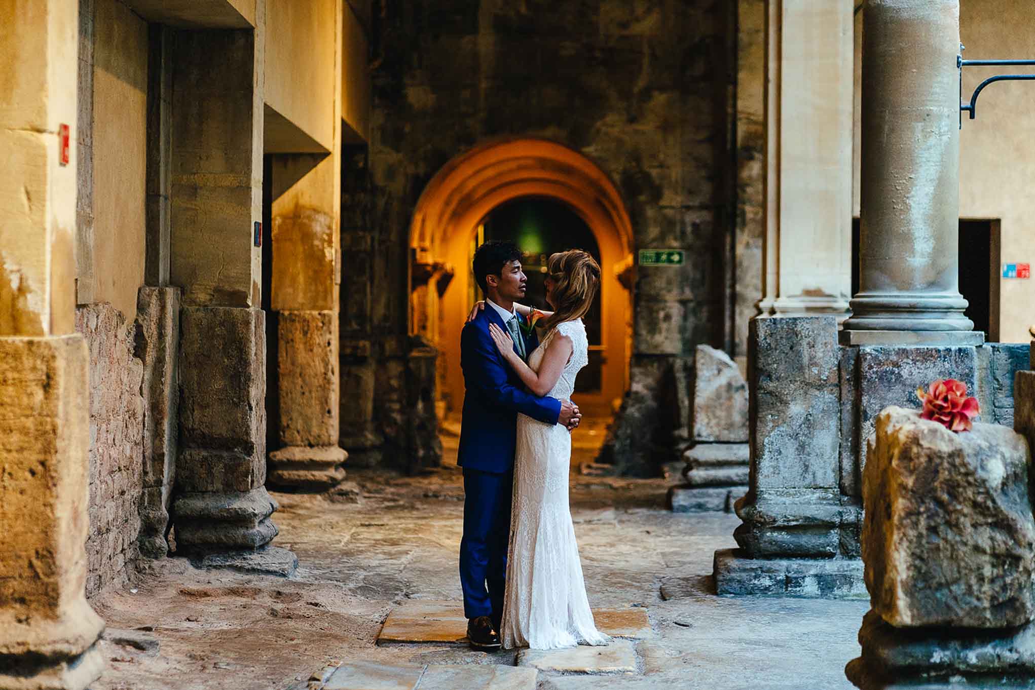 Wedding couple embrace with archway behind them