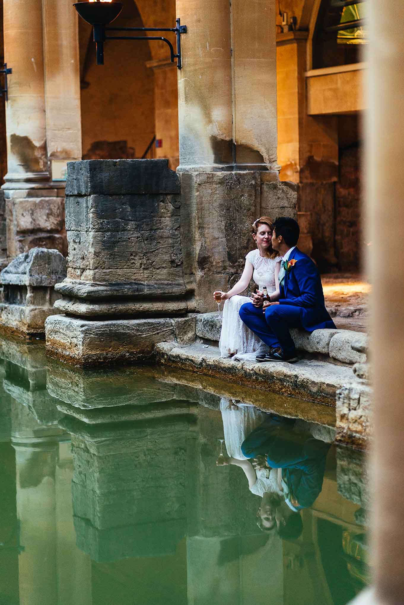 Couple seated on edge of the Great Bath holding a drink